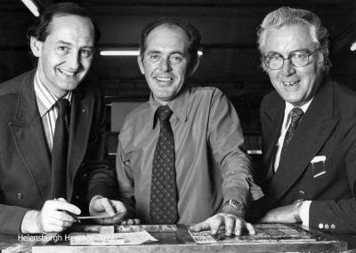 Editorial conference
Helensburgh Advertiser editor Donald Fullarton, sports editor Tony McGinley (who used the pen name Gare Clyde), and Advertiser founder and proprietor Craig M.Jeffrey beside the 'stone' where the hot metal pages were prepared at the East King Street printworks. Image c.1970.
