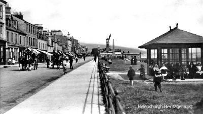 Seafront carriages
Children play around the William Street shelter on West Clyde Street, Helensburgh, as two horse-drawn carriages approach. Image circa 1909.

