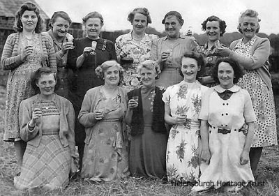 Farm ladies party
A FORMER Helensburgh woman now living in Shetland, Cathy Shearer, is trying to find out more about this photo of a group of women, including her granny, Barbara McAdam (back row 5th from left), who died in 1954 aged 67. The photo was taken between 1940-1954 by Alexandria photographers Leddy and Glen, probably in the Helensburgh area. At the time Barbara lived at either Callendoune Farm, Helensburgh, or Crossburn Cottage half a mile from the Cross Keys towards Luss. She would like to find out where and when the photo was taken, who the group of women are and what the occasion is. If you can help, please email the editor of this website.
