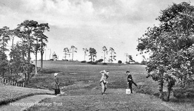Teeing off
A lady and the caddie watch as a player drives from the first tee at Helensburgh Golf Club. Image circa 1930.
