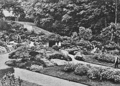 The Hermit's Well
Gardeners are at work and a family are having a picnic in this picture of the Hermit's Well in Hermitage Park. Image circa 1920, nine years after the park was created after the Town Council purchased the grounds from the Cramb family for Â£3,750. Legend has it that a hermit once lived in the park, and the Hermit's Well, with its copper ladle, granted a wish to those who drank from it. It is there to this day, but is not maintained in a good condition.
