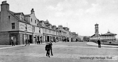Seafront crossing
The junction of West Clyde Street and Colquhoun Street, Helensburgh, as it used to be, with a cobbled walkway across the road to the pier. On the corner, where there is now a three-storey shop and office block, is Robert Brown's 'Cyclist's Rest Pierhead Vaults' public house. Image circa 1907.
