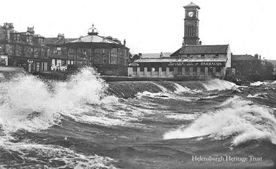 Stormy seafront
A view from the pier on a very stormy day at 3.35 p.m. looking towards the bandstand, the Granary when it was used as a garage, and the Old Parish Church. Image c.1920.
