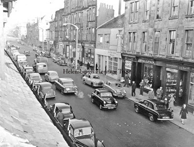 Sinclair Street shops
A view of the east side of Sinclair Street, between Clyde Street and Princes Street, circa 1950. The shops are C.G.Reid ironmonger, J.Rowan clothier, Birrell confectioner, the Tudor Garden Restaurant, A.Massey & Sons grocer, Alex Munro butcher, Peacocks hairdresser, Hargan's shoes, the entrance to the Waldie & Co. Ltd. garage, two unidentified shops, Ross shoes, Maclachlan bakers.
