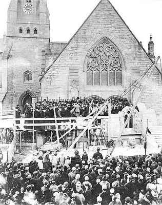 1892 Leiper Porch
A ceremony taking place during the construction of the William Leiper Porch at the West Free Church (now Helensburgh Parish Church) in mid-1982. The porch was built as a memorial to the Rev Alexander Anderson, minister of the church, who died in 1891. On the platform are two choirs and church dignitaries, and a large crowd are watching. On a ladder can be seen the name of local painting and decorating firm J.W.McCulloch who were in business in Colquhoun Square until a few years ago. Image by kind permission of Helensburgh Parish Church.
