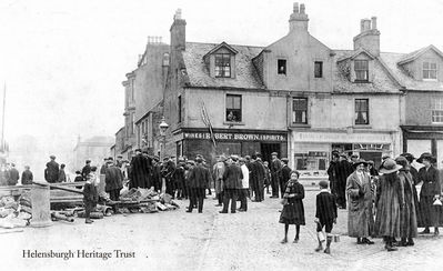 View from pier 1901
This view from the pierhead looking up Colquhoun Street was taken in 1901, but it is not known why a large crowd had gathered and what they were looking at. The shops are Robert Brown's wines and spirits and Lachlan McLachlan's very popular bakery. In 1929 the building which housed the two shops was demolished to allow the National Bank of Scotland to be built, and Lachlan McLachlan moved his business to Garelochhead where he worked until his death in 1951. Image supplied by Pat Drayton.
