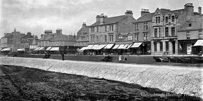 1912 West Promenade
People stroll on the seafront promenade and the West Clyde Streets shops have their sunshades down in this 1912 image.
