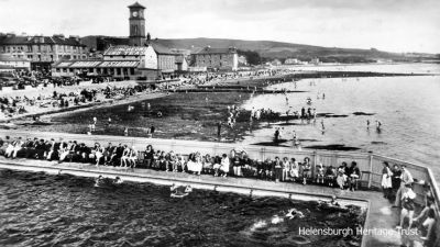 Busy Gala
Helensburg swimming pool is packed with spectators for a Helensburgh Swimming Club gala c.1936 — and the East Bay beyond is equally busy with sunseekers.
